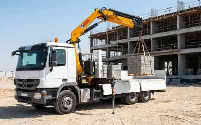 Crane-equipped truck relocating precast barriers on a UAE site