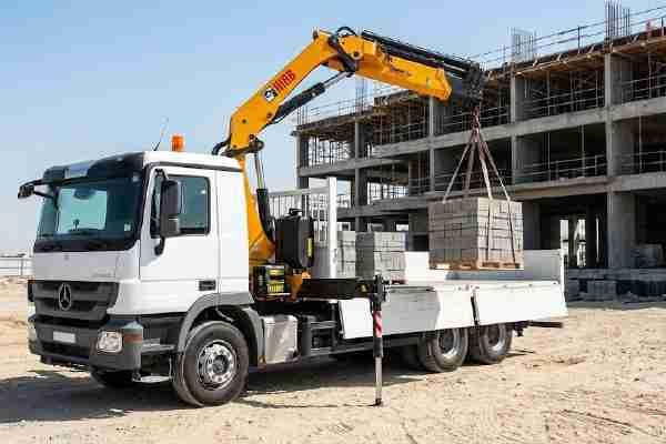 Crane-equipped truck relocating precast barriers on a UAE site