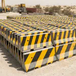 Stacked yellow-and-black precast concrete Jersey barriers at a UAE yard
