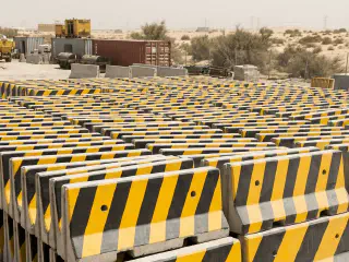 Stacked yellow-and-black precast concrete Jersey barriers at a UAE yard